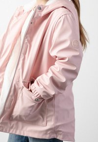 Jasnoróżowa wodoodporna kurtka z miękką polarową podszewką, z zamkiem z przodu, regulowanym kapturem, elastycznymi mankietami i kieszeniami bocznymi zapinanymi na zatrzask.