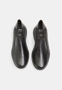 Chaussures en cuir noir à enfiler, avec une texture lisse, des panneaux latéraux élastiques et des semelles en caoutchouc striées pour l'adhérence et le confort.