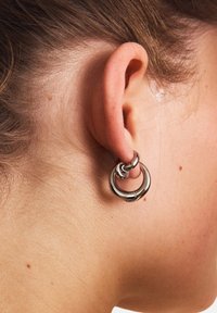 Pendientes de aros de plata con anillos entrelazados. Textura metálica suave, diseño minimalista con un acabado pulido.
