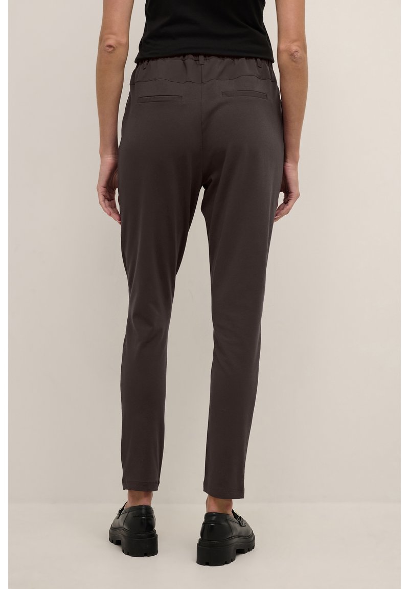 Tmavě šedé slim-fit kalhoty s elastickým pasem, které mají dvě zadní kapsy a hladký, lehký materiál. Nosené s černými botami.