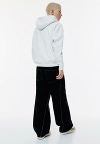 Felpa grigia con cappuccio dalla vestibilità rilassata, abbinata a pantaloni neri a gamba larga con cuciture a contrasto e una texture liscia.