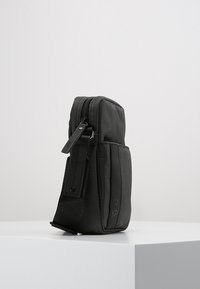 Compact black bag made of textured fabric with a zip closure, featuring a smooth panel and adjustable strap on the side.