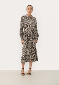 Sukienka koszulowa w print w panterę, z długimi rękawami, paskiem w talii i długości midi. Tkanina wydaje się gładka, w jasnobeżowym i czarnym kolorze.