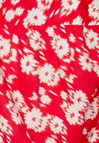 Rode jurkstof met witte bloempatronen en een ikat ontwerp. Het materiaal is glad, met plooien bij de taille voor extra textuur.