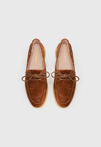 Brown suede loafers with a smooth texture, round toe, lace accents, and a tan rubber sole. Brand logo is displayed inside the shoes.