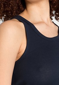 Canotta blu navy a costine con spalline larghe e una silhouette aderente. Il materiale sembra morbido con una leggera lucentezza, mettendo in risalto la texture del tessuto.