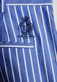 Niebiesko-biała materiał w paski, z haftowanym logo "TH" i koroną. Zawiera kontrastowe wykończenie oraz kieszeń.