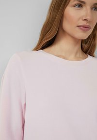 Hellrosa Sweatshirt mit rundem Ausschnitt und langen Ärmeln, mit glatter Textur und schlichtem Design, das Weichheit und Komfort betont.