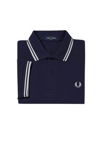 Camisa polo de color azul marino, doblada en plano, con una tapeta de dos botones, cuello a rayas blancas y logo blanco bordado en el pecho.