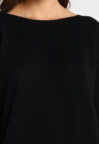 Mustapintainen, leveäkauluksinen neulepusero, jossa on pitkät hihat ja joka on valmistettu pehmeästä kankaasta. Siinä on rento istuvuus ja minimalistinen muotoilu ilman näkyviä kuvioita tai korostuksia.