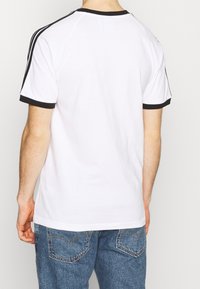 Bílá tričko s černým lemem kolem výstřihu a rukávů, se černými pruhy podél ramen. Nosené s modrými džíny.