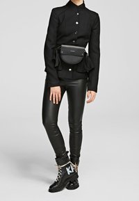 Veste noire ajustée avec des accents volants, fermeture à boutons, associée à un pantalon en cuir noir brillant et des bottes à lacets avec des lettres contrastées.