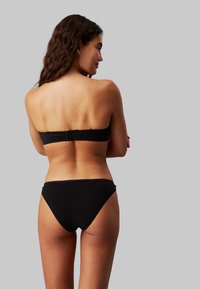 Set di bikini nero con top senza spalline e chiusura a clip, e slip a vita bassa classica. Texture liscia e design minimalista.