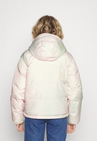 Pružená bunda v iridescentnej ružovej a zelenej farbe, s veľkou kapucňou, elastickými manžetami a rovný pás; hladká, lesklá textúra látky.