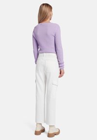 Top lungo a maniche opzionali in tessuto lilla abbinato a pantaloni cargo bianchi a vita alta. Stivaletti platform color cammello notevoli completano l'outfit.