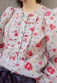 Durchsichtige Bluse mit roten Blumen und lila Polka-Dots, mit Rüschen vorne und dekorativen Juwelenknöpfen. Strukturiertes Gewebe.