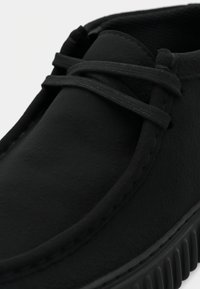 Scarpa slip-on nera in suede con punta rotonda, lacci tono su tono e lati testurizzati, dotata di una suola in gomma con scanalature per grip.