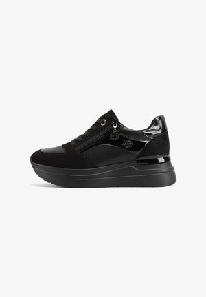 Zapatillas negras que combinan materiales lisos y texturizados, con un acento de cremallera y una suela gruesa para mayor altura.