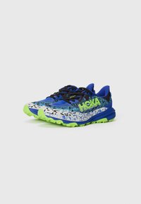 Baskets bleu et noir avec un design éclaboussé, des accents verts, des lacets noirs et une semelle texturée pour une meilleure adhérence. Logo HOKA en vert vif.