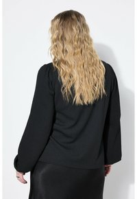 Maglietta nera a maniche lunghe con tessuto testurizzato, spalle arricciate e una vestibilità leggermente rilassata, abbinata a una gonna nera liscia.