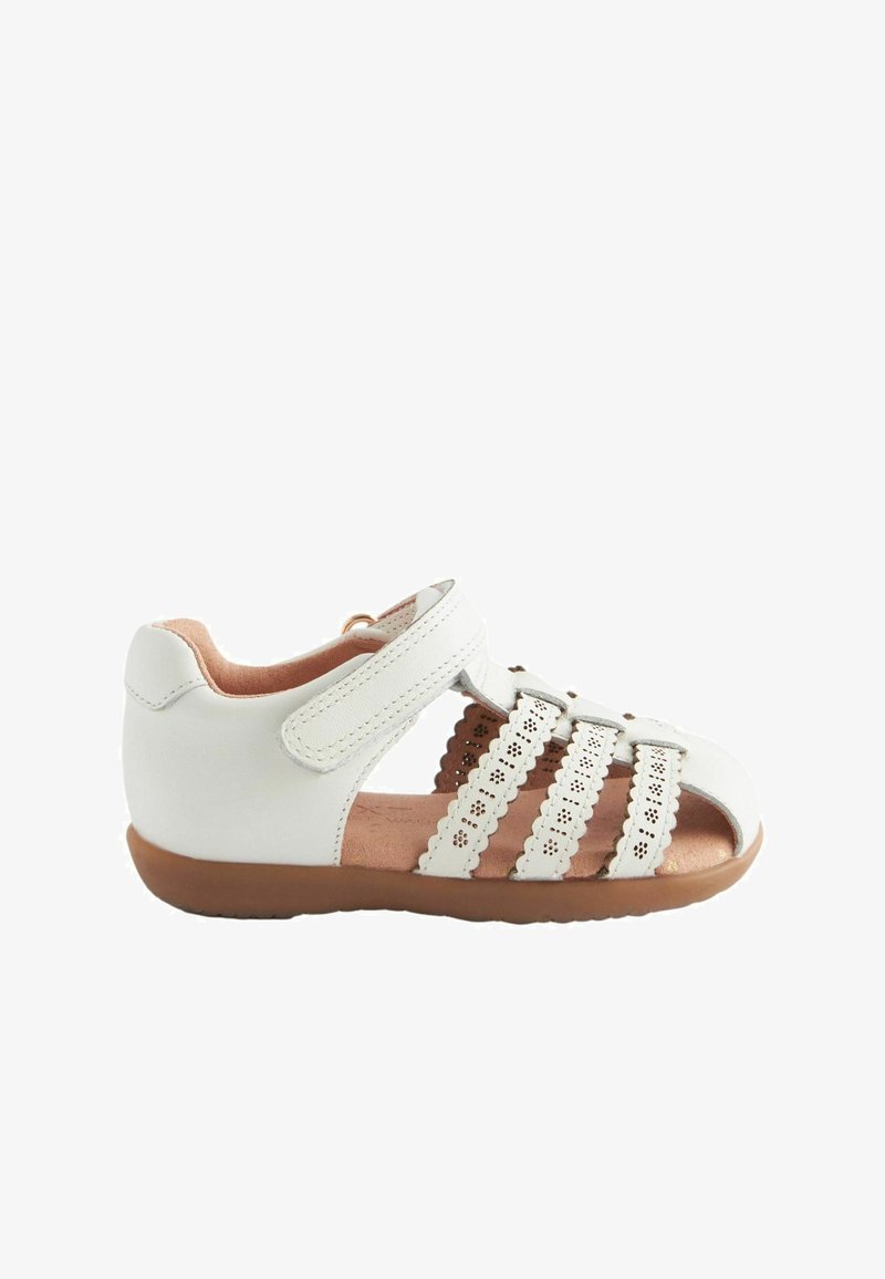 Białe skórzane sandały z otwartym palcem i piętą. Posiadają dekoracyjne wycięcia na paskach oraz zapięcie na rzep. Brązowa gumowa podeszwa, wyściełana wkładka.