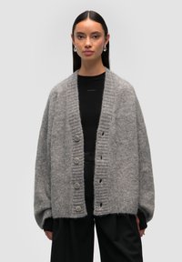 Szary wełniany kardigan z żebrowanym wykończeniem, oversize'owy krój i zapięcie na pięć guzików. Miękka tekstura, długie rękawy, zestawiony z czarną bluzką.