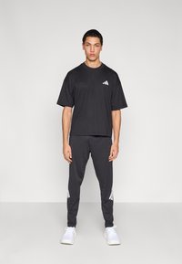 Černé tričko s krátkým rukávem a bílými logovými prvky, doplněné o tmavé sportovní kalhoty s bílými proužky a bílé sportovní boty.