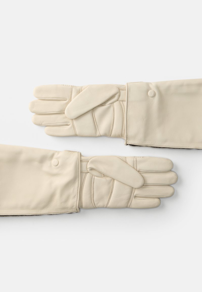 Gants en cuir crème avec un motif matelassé, présentant un design repliable et des fermetures à pression. Texture lisse et ouvertures pour les doigts visibles.
