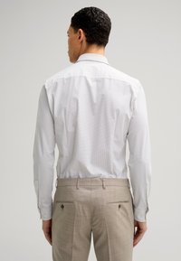 Camicia bianca con un discreto motivo a rete, maniche lunghe e polsini con bottone. Abbinata a pantaloni beige chiaro con tasche posteriori e bottoni.