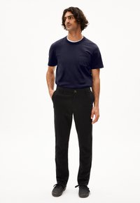Marineblauw t-shirt met korte mouwen, ronde hals en borstzak, gecombineerd met zwarte chino's en grijze veterschoenen. Eenvoudig, strak ontwerp.