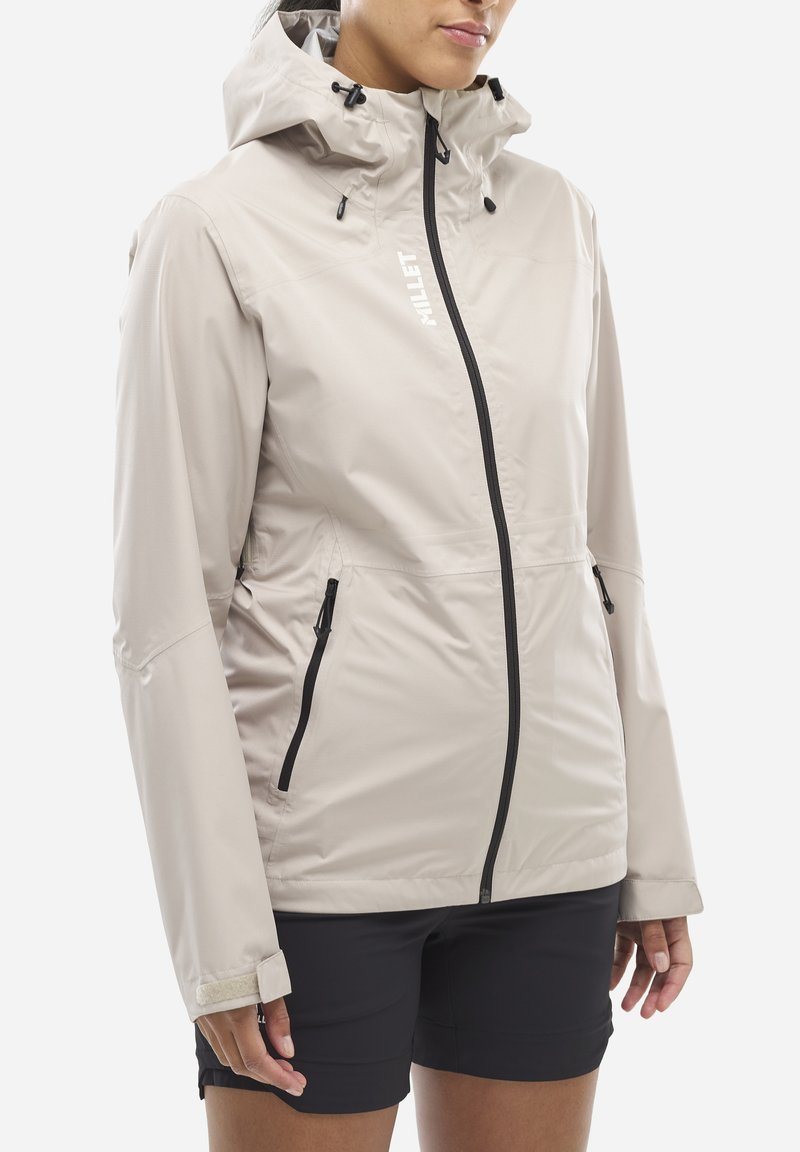 Veste imperméable beige clair avec une capuche ajustée, zips noirs et poches latérales. Texture lisse, poignets ajustables et branding minimal.