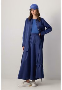 Blauwe button-up shirt over een blauwe top, gecombineerd met een blauwe geplooide rok. Bevat een baseballpet en witte sneakers. Zacht materiaal.