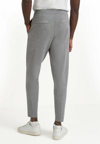 Grijze joggerbroek met een tapered fit, voorzien van achterzakken en stiksels, gecombineerd met witte sneakers en geribde sokken.