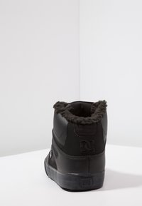 Svarte høyhælte sneakers laget av teksturert lærmateriale med kunstig pelstrim rundt ankelen. Har logo-detall på hælen og gummisåle.