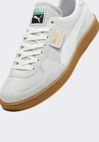 Szare zamszowe sneakersy z białymi skórzanymi akcentami i gumową podeszwą. Zawierają białe sznurówki oraz zielono-czarną markową naszywkę na języku.