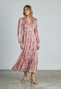 Langes Blumenkleid mit V-Ausschnitt, Puffärmeln und tailliertem Detail. Lila- und Gelbmuster auf leichtem Stoff mit einem fließenden Rock.