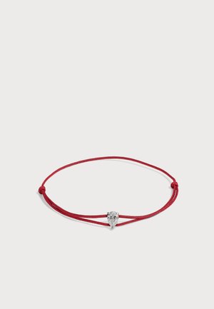 Bracelet en cordon rouge avec des nœuds réglables, présentant une pierre précieuse claire en forme de poire dans un sertissage argenté au centre.