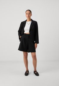 Svart blazer med en enkel knapp, i kombination med svarta plisserade shorts. En åtsittande vit crop top fulländar outfitten. Enkla svarta skor.