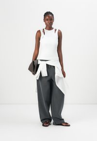 White tank top with cut-out shoulder straps, gray wide-leg pants, and a white layered shirt tied at the waist. Brown clutch and black sandals.