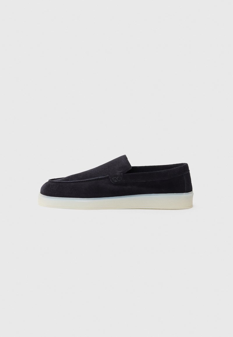 Tumesinine suede slip-on kingad sileda viimistlusega, ümarate varvastega ja madala valge kummitaldaga. Minimalistlik disain, ilma nähtava riistvara või mustriteta.