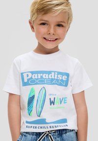 Biała bawełniana koszulka z kolorowymi grafikami desek surfingowych, niebieski napis "Paradise OCEAN" oraz "CATCH A WAVE", luźny krój.