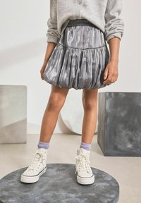 Silberner metallischer Bubble-Rock mit elastischem Bund, kombiniert mit weißen High-Top-Sneakern und lavendelfarbenen Crew-Socken. Strukturiertes Gewebe mit Falten.