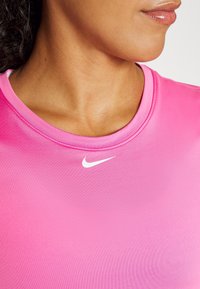 Camiseta deportiva rosa con una textura suave, que presenta un escote redondeado y un pequeño logo blanco de Nike en el centro.