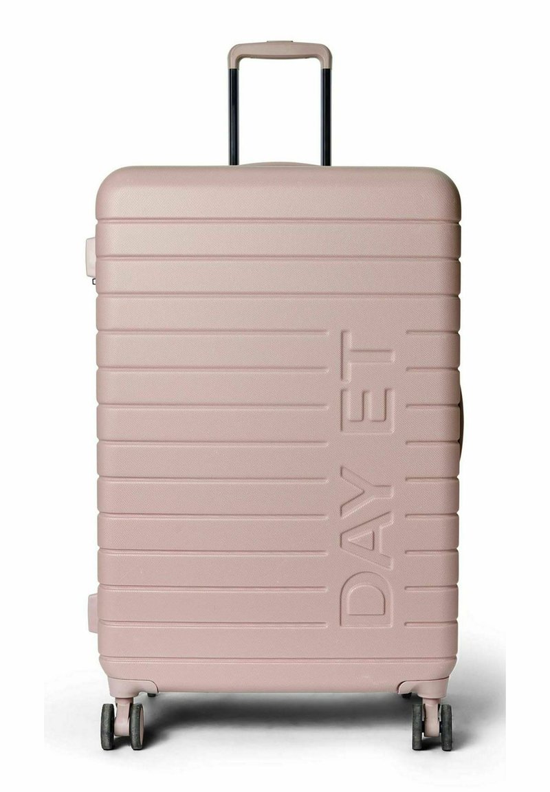 Valise rigide de couleur rose clair avec texture nervurée horizontale, poignée télescopique et quatre roues pivotantes. Nom de la marque affiché à l'avant.