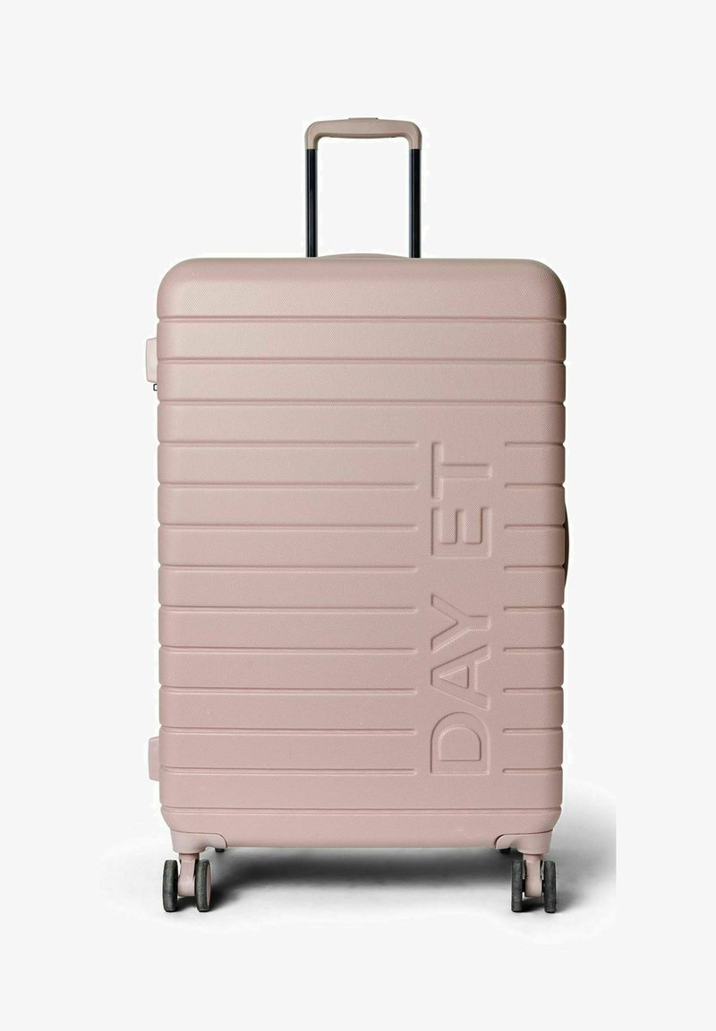 Valise rigide de couleur rose clair avec texture nervurée horizontale, poignée télescopique et quatre roues pivotantes. Nom de la marque affiché à l'avant.