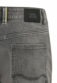 Grå denim jeans har et sort label med "camel active" brandnavn, gul syning og en baglomme med stikdetaljer.