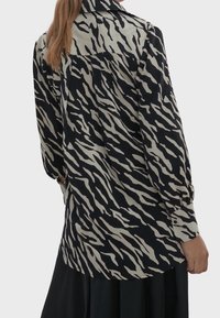 Long-sleeve shirt in black and cream with a wavy animal print. Features a collar, button cuffs, and a relaxed fit design.