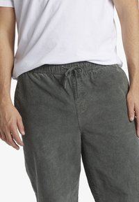 Pantalones de pana gris con cintura elástica y cordón. La tela tiene una textura acanalada vertical; los bolsillos no son visibles.