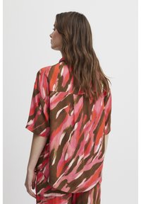 Camicia a maniche corte in tessuto leggero con un vivace motivo astratto nei colori rosa, marrone e arancione, dotata di una chiusura a bottoni e di una yoke posteriore.
