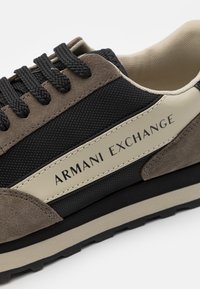 Sportsko sneakers med svart tekstiloverdel og brune semskede detaljer, beige lærlogo, teksturerte lisser og en robust gummisåle.